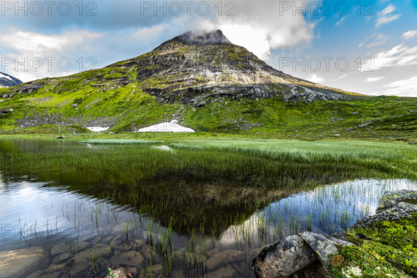 Mountain lake with mirror-like water and green slopes, peaceful and calm under a blue sky