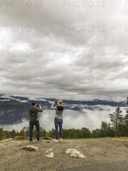 Utvik, Vestland, Norway, Two people photograph a foggy landscape with mountains and clouds with their smartphones