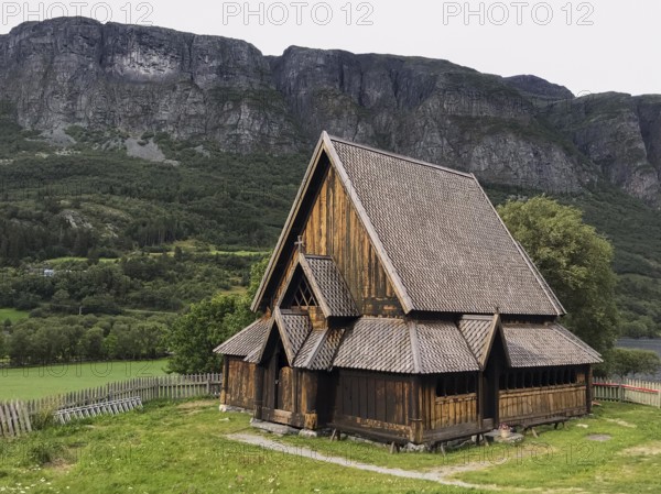 Øye, Innlandet, Norway, Traditional stave church in front of steep mountains in rural surroundings, traditional wooden church in front of impressive mountain cliffs in a quiet landscape
