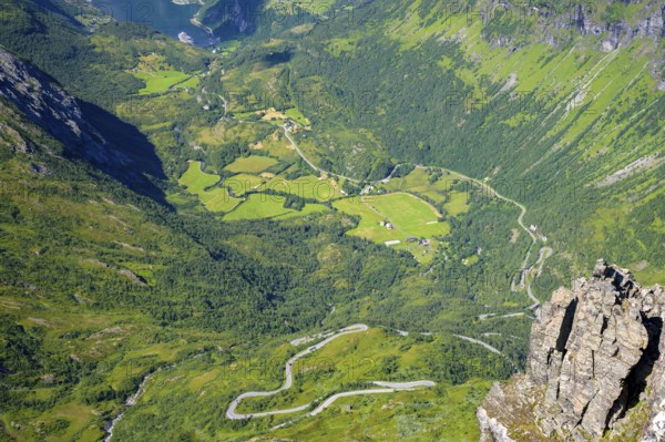 Geiranger, Møre og Romsdal Province, Norway, Winding road through green fields in a mountain valley with the Geiranger Fjord, highest fjord view in Europe from the Geiranger Skywalk
