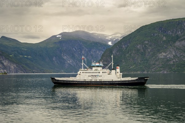Valldal, Møre og Romsdal province, Norway, Fram Geiranger ferry in calm water surrounded by high mountains under a cloudy sky