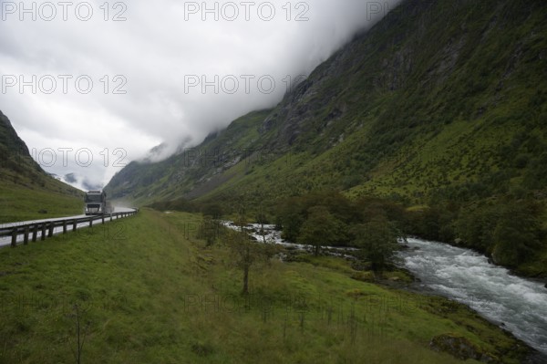 Byrkjelo, Vestland, Norway, truck on road in valley with towering mountains and a river next to it