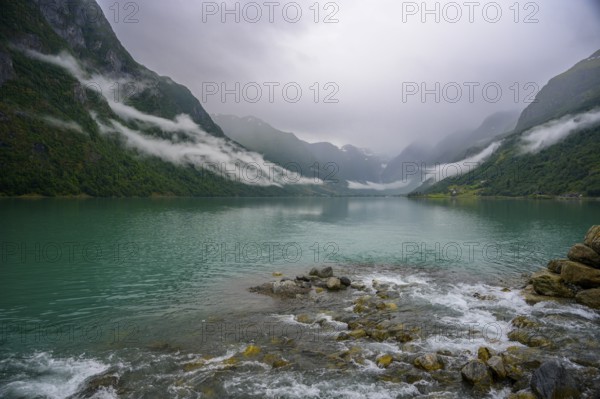 Olden, Vestland, Norway, Tranquil fjord landscape with mountains and cloudy sky, surrounded by green hills near Brikdalsbreen glacier