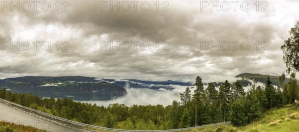 Utvik, Vestland, Norway, panoramic view of foggy mountain slopes and a dense forest under cloudy sky, wide view of a foggy landscape with forest and lake under a cloudy sky