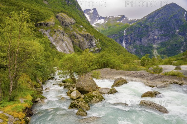 Briksdalsbre, Vestland, Norway, fast-flowing river through green valley with rocks and distant waterfalls on Brikdalsbreen glacier