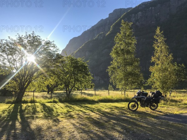 Lysebotn, Rogaland Municipality, Norway, sunrise illuminates a green landscape with a motorcycle in the foreground