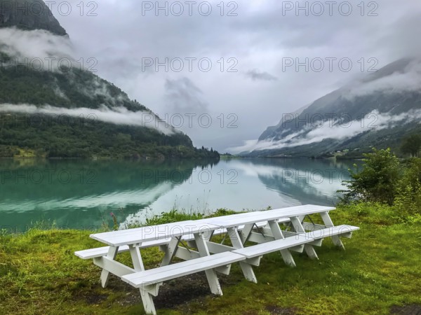 Olden, Vestland, Norway, white picnic table at a lake with mountains and low-hanging clouds in the background, valley near Brikdalsbreen glacier