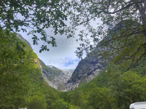 Oldedalen, Vestland, Norway, view through trees of an impressive mountain gorge under a calm sky of the Brikdalsbreen glacier