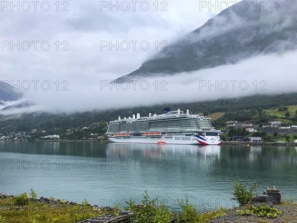 Olden, Vestland, Norway, Large cruise ship anchors in a fjord with forested mountains and clouds of fog