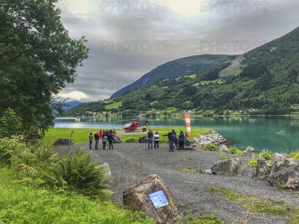 Loen, Vestland, Norway, fjord scenery with gathered people Cruise tourists waiting for a sightseeing flight over Jostedalsbreen and a helicopter
