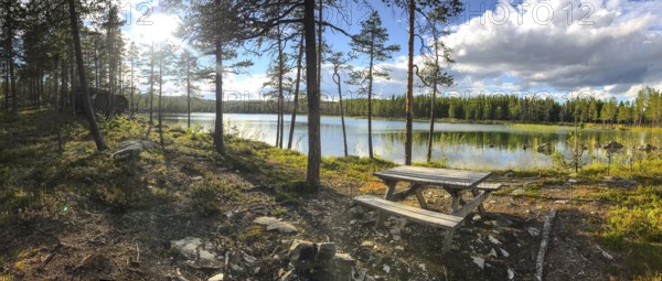 Storsjö Kapell, Jämtlands län, Sweden, panorama of a sunlit forest lake with picnic table in the foreground