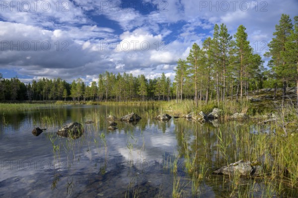 Torsborg, Jämtland County, Sweden, reflecting lake with rocks and forest in sunshine under cloudy sky