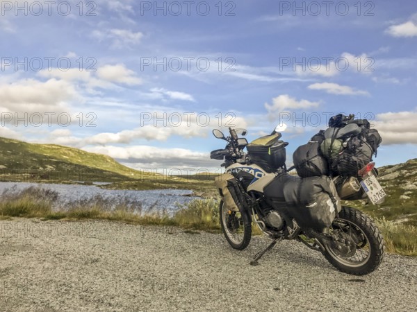 Haugastøl, Viken, Norway, A loaded motorcycle on a road with lake and mountain views in the background in Hardangervidda