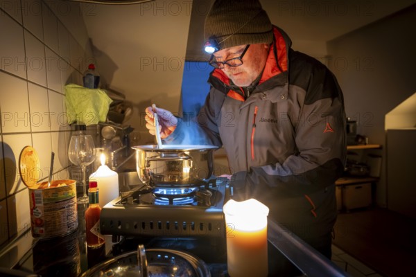 Symbolic picture blackout, extensive, prolonged power failure, in private settings, without electricity, heating, water, cooking in the kitchen, heating food with a gas-powered camping stove, which is also approved for indoor use