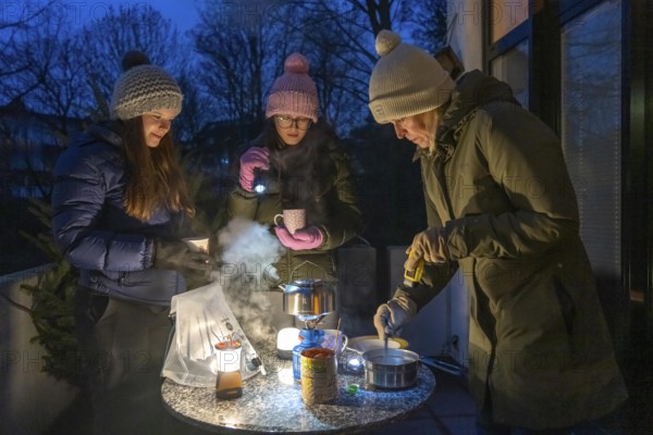 Symbolic picture blackout, extensive, prolonged power failure, in private surroundings, without electricity, heating, water, cooking, heating food and water with a gas-powered camping stove, on the balcony