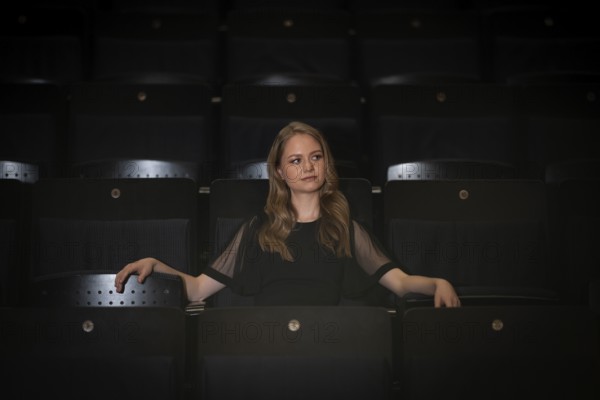 Young woman, pianist, in evening dress, sitting on chair in audience area, Stuttgart, Baden-Württemberg, Germany
