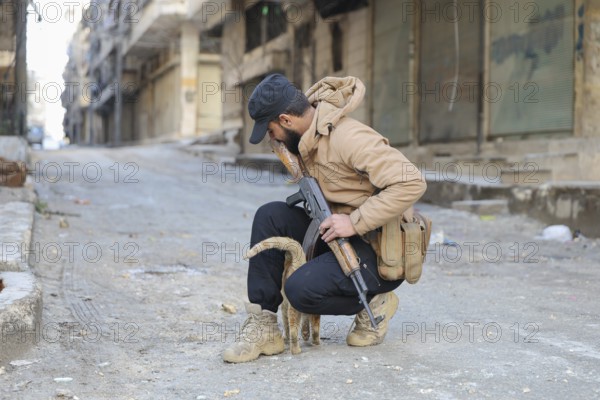 In Aleppo, Syria on January 10, 2026, a Syrian Army soldier crouches to pet a stray cat in the street following intense battles with SDF forces in the Sheikh Maqsoud and Ashrafieh neighborhoods after the withdrawal of Kurdish groups towards eastern Syria, Aleppo, Sheikh Maqsood, Syria