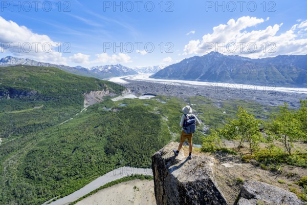 Young man on a rocky outcrop enjoying the view, view of impressive mountain scenery with Matanuska glacier and glaciated mountain peaks, Lion's Head, Chugach Mountains, Alaska, USA