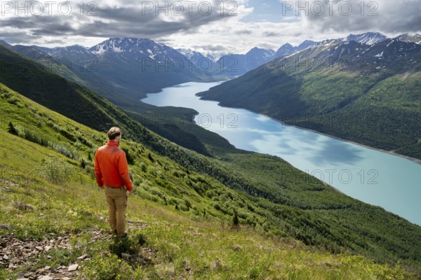 Mountaineer enjoys views of blue lake and mountains on Twin Peaks Trail, Eklutna Lake, Chugach Mountains, Chugach State Park, Alaska, USA