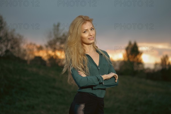 Cheerful woman with blonde hair stands with her arms crossed on a heel during sunset. Retreat in a calm environment