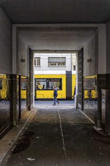 View through a corridor to the backyard onto Chässeestraße with passengers and moving tram, Berlin, Germany
