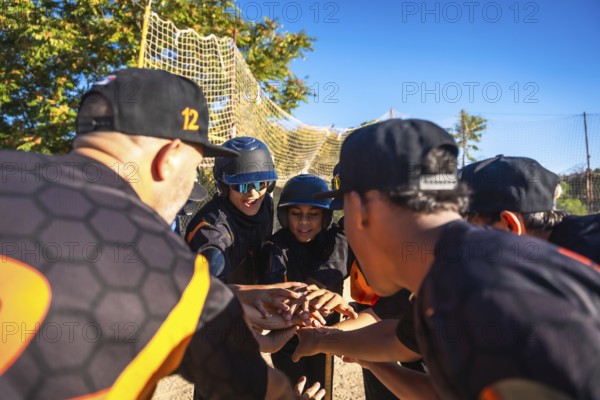 Baseball coach and diverse youth team link hands in a motivating pre game huddle on a sunny field, showing teamwork, leadership, focus and community spirit before practice