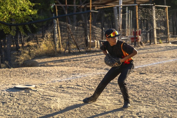 Young boy in cap and sunglasses poised to catch a baseball with his glove on a sunny dirt field during practice or a youth game, focused and ready for action