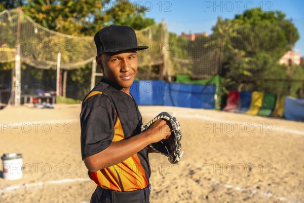 Confident young baseball player stands on dusty field gripping his glove, smiling at the camera and ready for the game, showcasing focus, dedication and outdoor athletic spirit