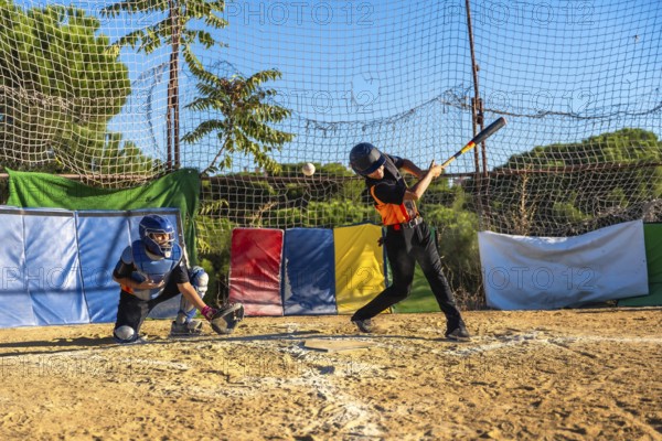 Young baseball players honing their skills, with a batter swinging a bat to hit a flying ball and a catcher ready behind home plate during an outdoor practice session