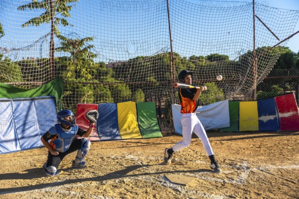 Young baseball players focusing on sport, with a batter hitting a baseball and a catcher ready behind the plate during an outdoor practice session, demonstrating youth sports engagement