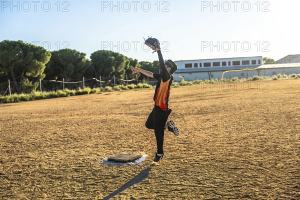 Young baseball player in uniform and glove jumping to catch a flying ball on a sunny dirt field, demonstrating effort, action, and determination in sport