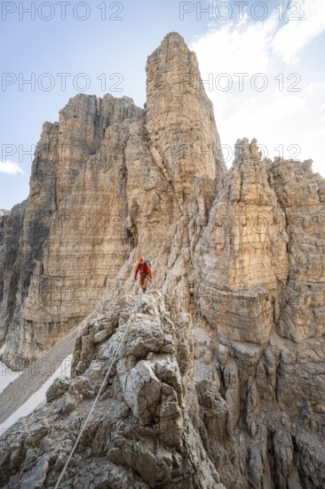 Mountaineer climbs an exposed rock in the secured Via Ferrata Bocciere Centrale via ferrata, spectacular rock towers in the back, Brenta Mountains, Brenta-Adamello Natural Park, Trentino, Italy