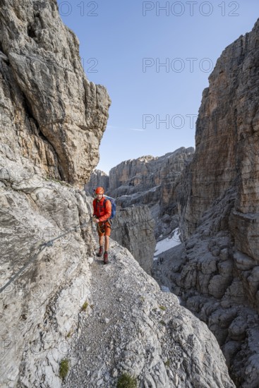 Mountaineer climbs an exposed rock band in the secured via ferrata Bocciere Centrale, Brenta Mountains, Parco Naturale Brenta-Adamello, Trentino, Italy