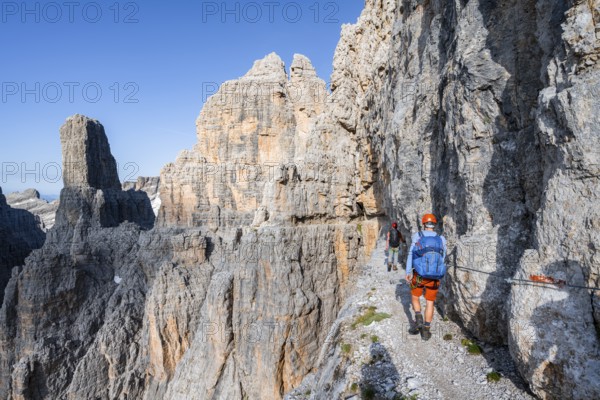 Two mountaineers on an exposed rock band in the secured Via Ferrata Bocciere Centrale via ferrata, spectacular mountain landscape with steep rocky peaks, Brenta Mountains, Parco Naturale Brenta-Adamello, Trentino, Italy
