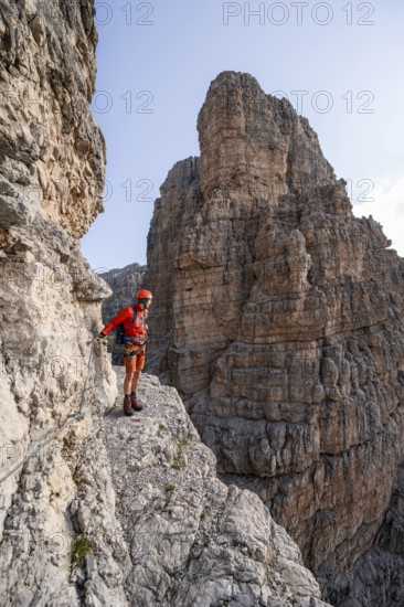 Mountaineer climbs an exposed rock band in the secured Via Ferrata Bocciere Centrale via ferrata, spectacular mountain landscape with steep rock faces, Brenta Mountains, Parco Naturale Brenta-Adamello, Trentino, Italy