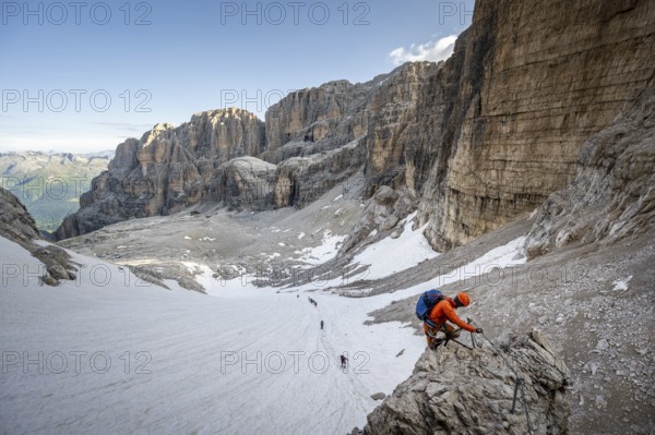 Mountaineer climbs on an exposed rock in the secured Via Ferrata Bocciere Centrale via ferrata, view of snow remains from the Vedretta del Sfulmini glacier, Brenta Mountains, Parco Naturale Brenta-Adamello, Trentino, Italy