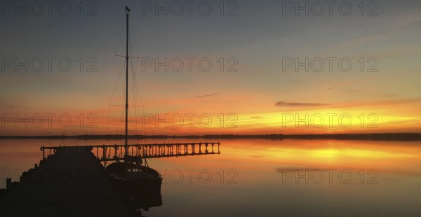 Tranquil Dümmer See with dock and sailboat at sunset, warm colors and calm atmosphere, Lembruch, Dümmer nature park Park, Lower Saxony, Germany