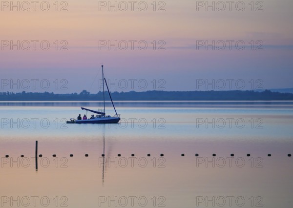 Sailing boat glides across quiet Dümmer Lake in the colors of a sunset, Dümmer nature park Park, Lower Saxony, Germany