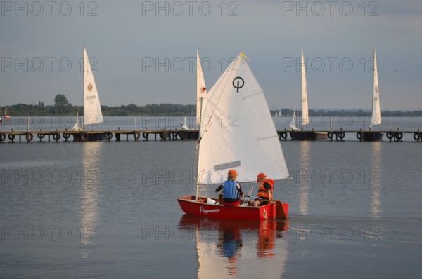 Two children 6 and 10 years old in a small red sailboat Optimist Jolle Opti on Lake Dümmer in calm skies, Dümmer nature park Park, Lembruch, Lower Saxony, Germany
