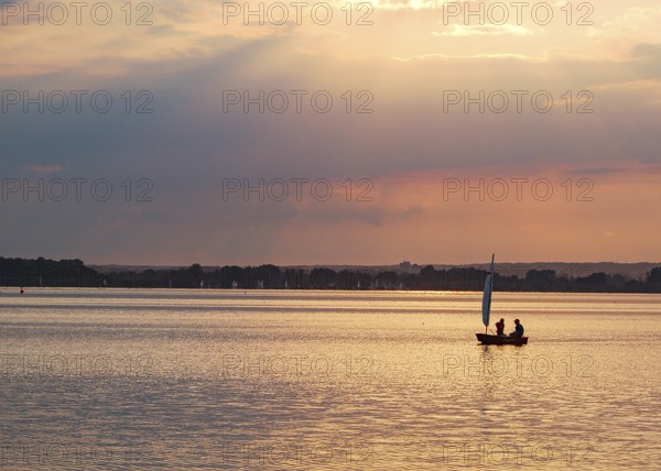 Two children 6 and 10 years old in a small red sailboat Optimist Jolle Opti on the Dümmer at golden evening light, Dümmer nature park Park, Lembruch, Lower Saxony, Germany