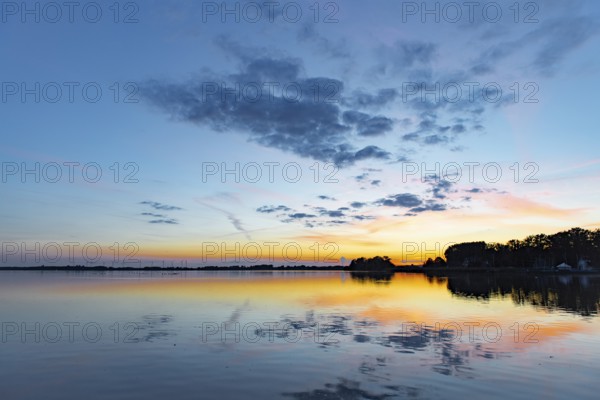 Sunset over quiet Dümmer See with colorful sky and clouds reflecting in the water, Lembruch, Dümmer nature park Park, Lower Saxony, Germany