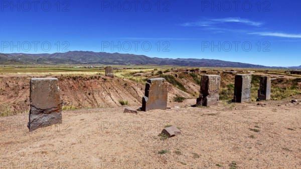 Standing stone monoliths overlook a vast open area with mountain backdrop, the archaeological site with the ruins of Tiwanaku in Bolivia