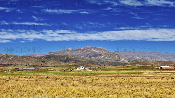 Wide fields in front of a mountain range under a cloudy sky, The Altiplano landscape in the Andes of Bolivia