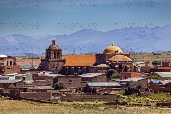 Historic church in a village with brick red roofs against a mountain backdrop under clear skies, The city of Tiwanaku near the ruins of Tiwanaku in Bolivia