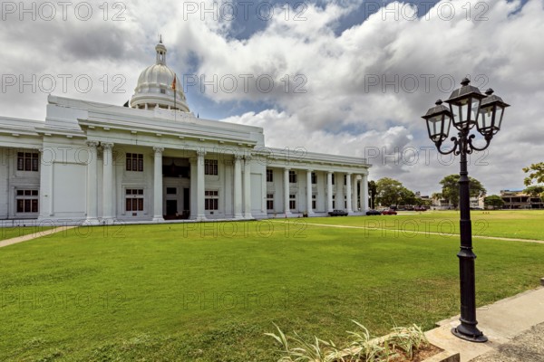 A white building with dome and pillars surrounded by green lawn under cloudy sky, Colombo Sri Lanka City Council