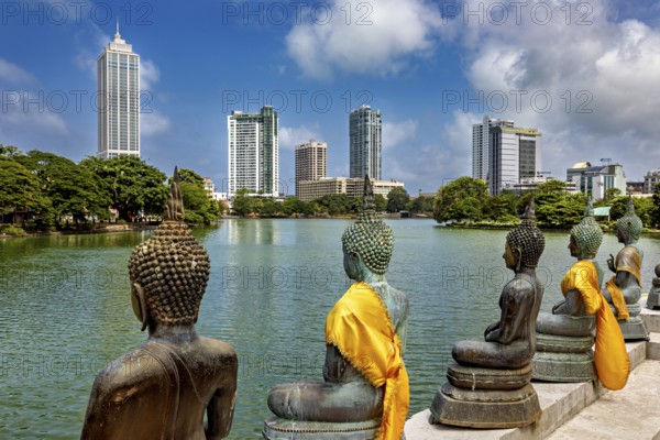 Bronze Buddha statues with yellow cloths look at the skyline of a city, the Seema Malaka temple with the Buddha statues in Colombo Sri Lanka