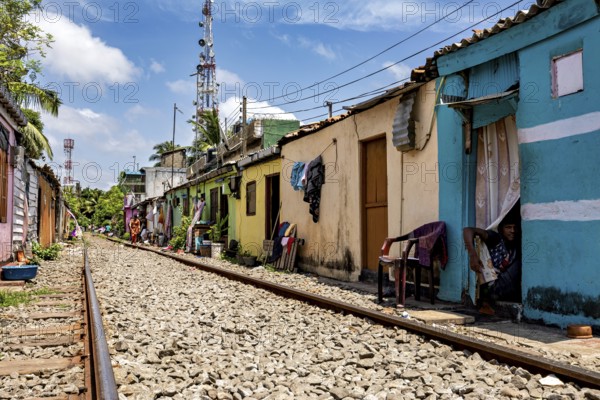 Tracks lead through residential area with bright houses and chairs outside under sunny skies, railway line in the historic Slave Island district in Colombo Sri Lanka