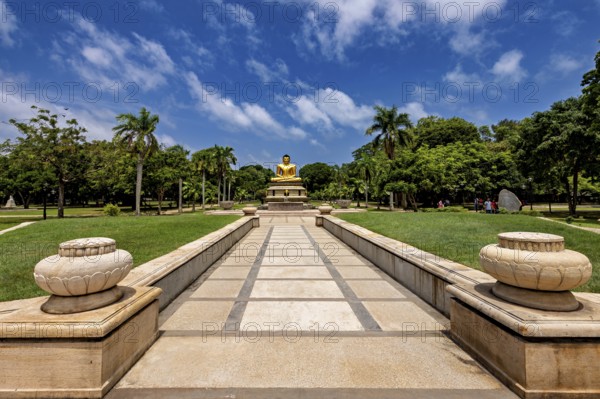 Quiet park with centrally placed Buddha statue and stone path under blue sky, The Golden Buddha in Colombo Sri Lanka City Park