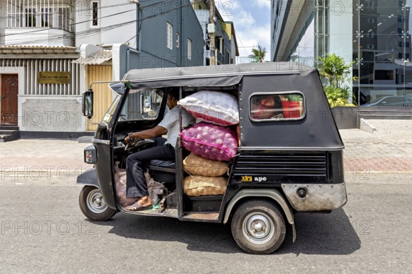 A loaded car rickshaw drives through an urban environment in sunny weather, tuk tuk transport in the streets of Colombo Sri Lanka