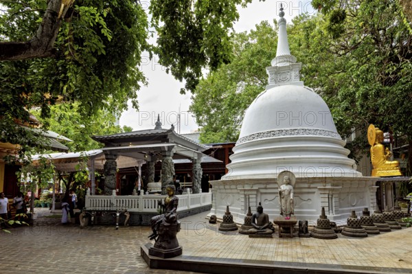 A Buddhist temple complex with a white stupa surrounded by Buddha statues and lush greenery, The Gangaramaya Temple in Colombo Sri Lanka